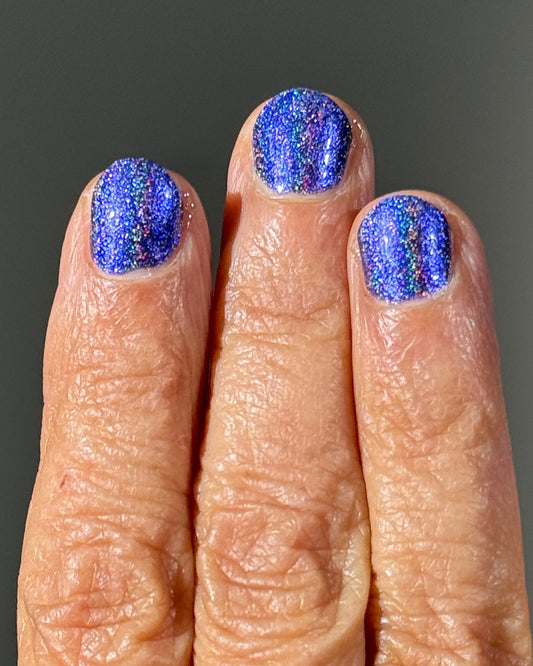 Close-up of a hand with blue glittery nail polish on a dark background preview